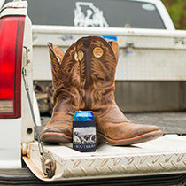 Leather boots in the back of a pickup truck, with a Straight Up Souther drink koozie