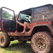 A pair of legs stretch out from the open door of a mud-spattered Jeep