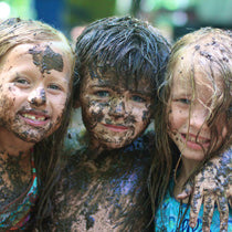 Three children smile for the camera while covered in mud