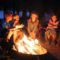 Four kids warm themselves by a campfire at night