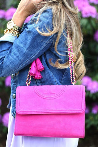 woman holding neon tory burch bag she is wearing denim 