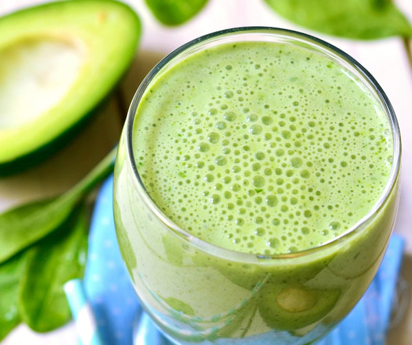 glass of green smoothie with avocado in the background