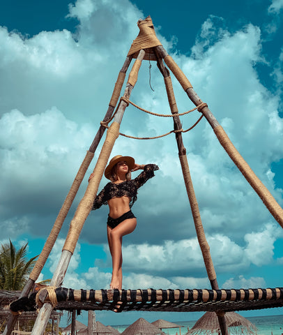 Youma Leth wearing a black swimwear and enjoying the sunshine on a wooden tipi in Tulum Mexico