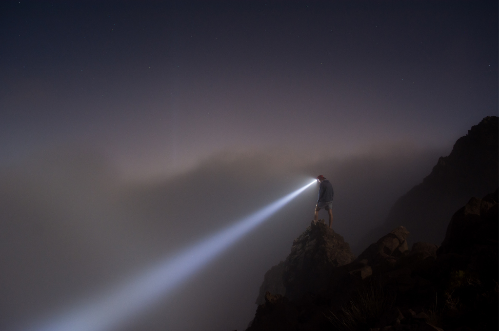 Person standing on mountain with headlamp on. It is just after sunset and getting dark