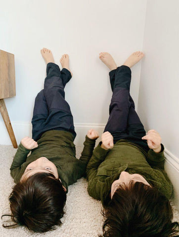 Two kids laying on the grown with their legs up the wall, wearing Jackalo.