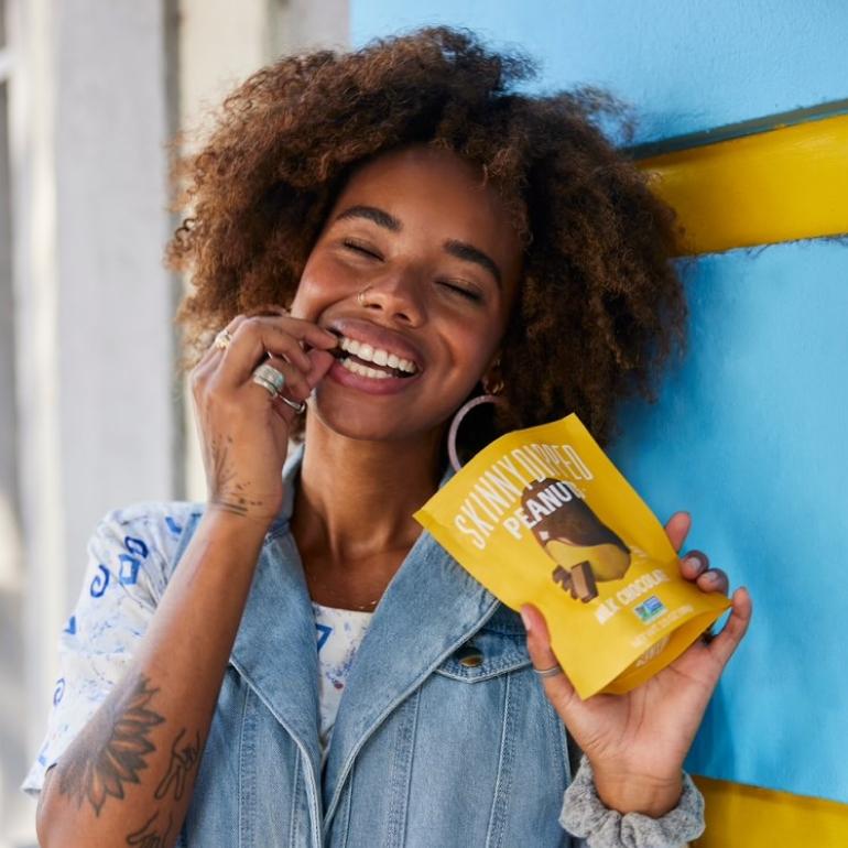 Girl snacking on SkinnyDipped Milk Chocolate Peanuts with a smile.