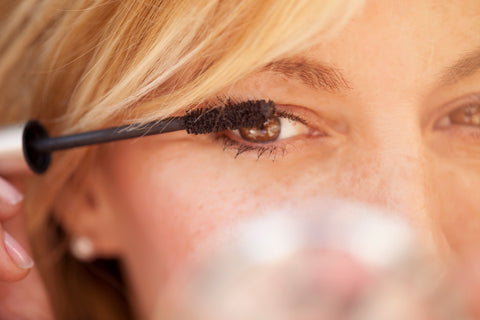 Blonde woman applying mascara to eyelashes