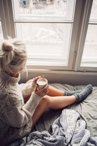Cozy blonde woman in a chunky sweater gazing out window with hair in bun