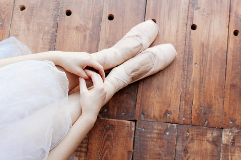 Ballerina sitting on wooden floor in ballet slippers