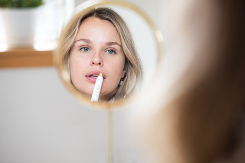 Blonde woman looking in mirror applying Ogee organic Sculpted Lip Oil