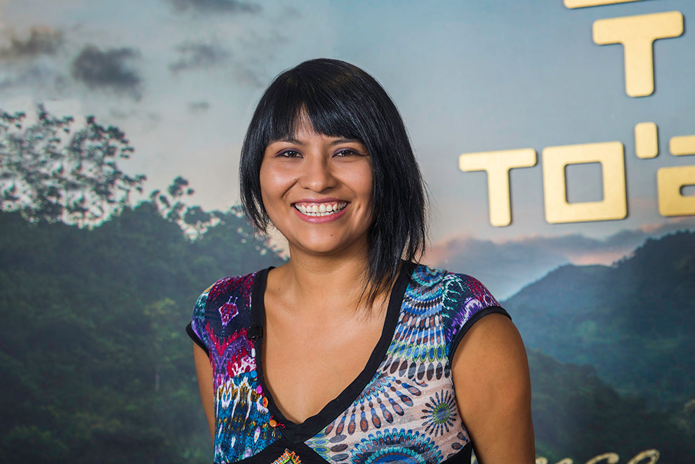 Photograph of To’ak’s general manager, Dennise Valencia. She is facing the camera and smiling, with a To’ak backdrop behind her.