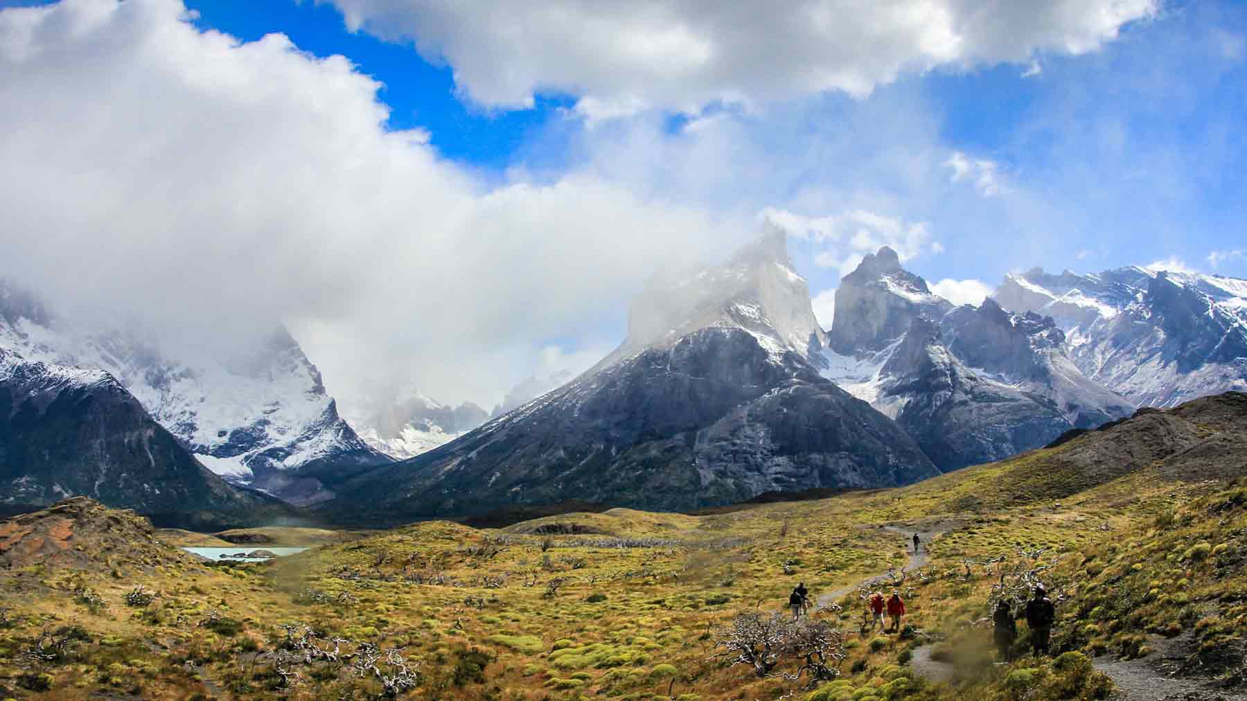 Looking towards the cloud shrouded Torres del Paine across yellow grass covered hills, part of the travel that inspired the creation of Asmuss clothing