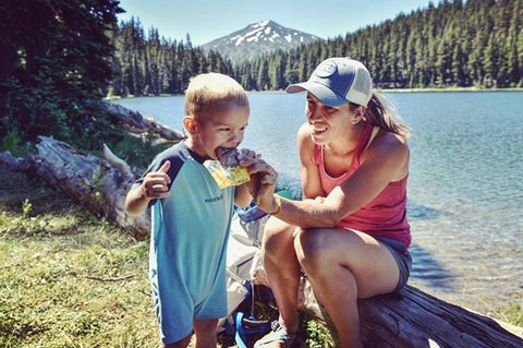 Mom and Toddler eat Bobo's Oat Bars by the lake while camping. 