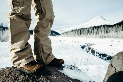 Hiker in full zip rain pants stands in the foreground in front of an icy peak.