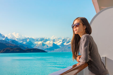 A woman on an Alaskan cruise looks out over the water with snow-capped peaks in the background.