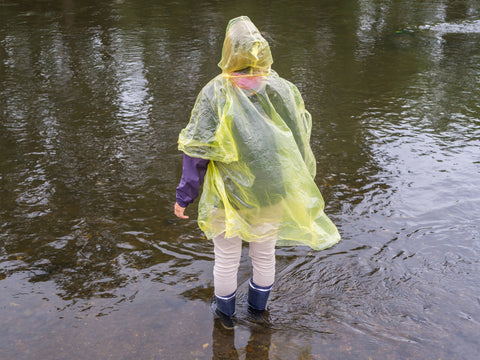 A person in a poncho stands on the edge of a puddle.