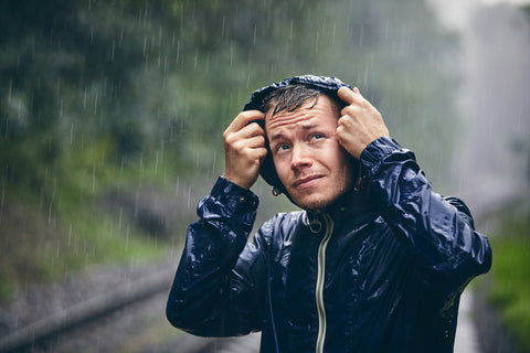 A man in a rain jacket holds his hood and watches the weather. 