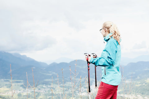 Hiker in full zip rain pants and a rain jacket overlooks a vista. 