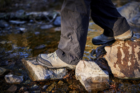 Close-up shot of full zip rain pants on a hiker crossing a stream.