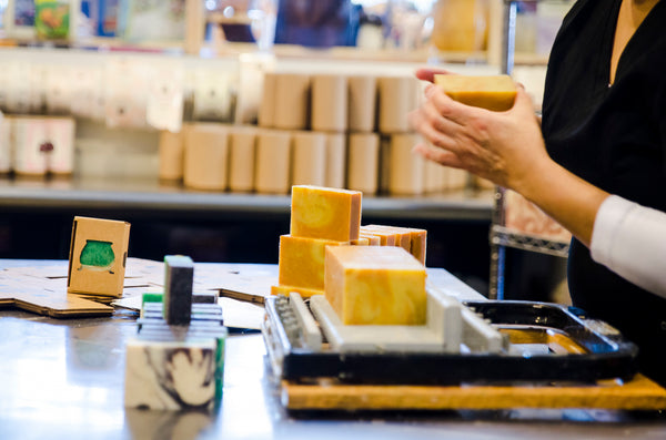 a work table with soap and soap cutter with someone handling a soap bar on the right