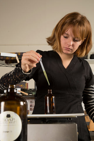 a young woman using a dropper to add essential oil to a dark bottle