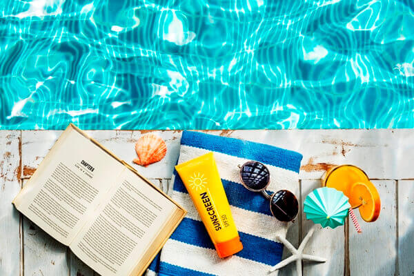 Sunscreen, towel, and books beside the pool