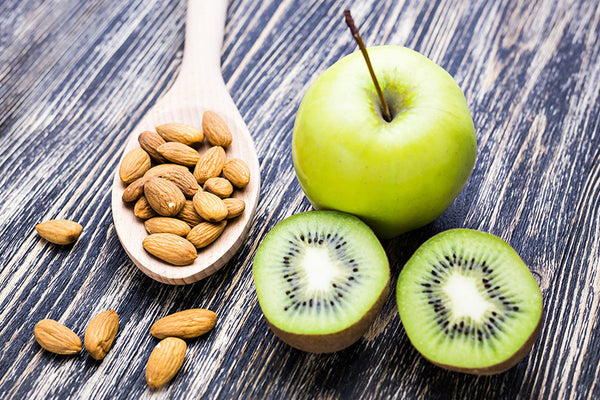 Green apple, sliced kiwi, and a spoon of almonds on a wooden table