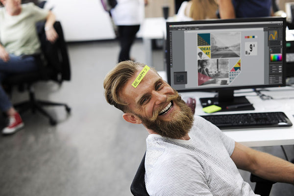 Man laughing at work, paper with 'be happy' note pasted on his forehead