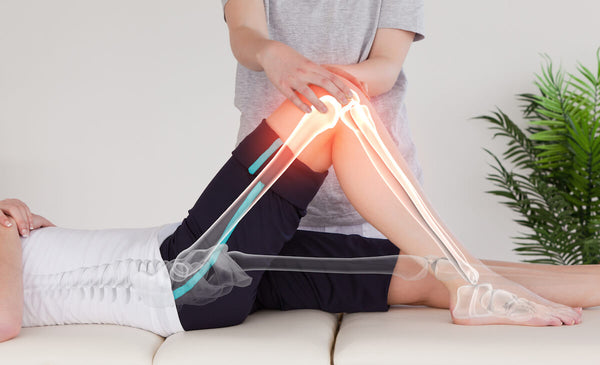 Image of a man on his back getting his knee worked on by a physical therapist. The image is showing the symptoms of knee pain and tight calves.