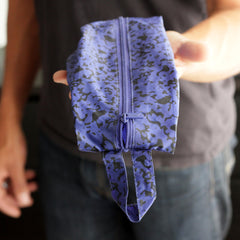 Person holding a blue zippered pouch with a black abstract pattern and a loop handle at the end