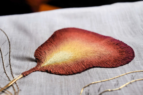 Side view of finished petal hand embroidered in reds and golds using long and short stitch