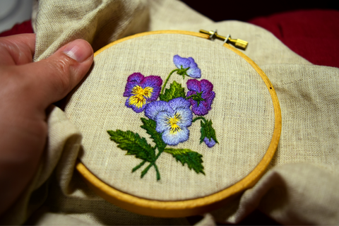 Embroidered posy of pansies on oatmeal linen. Purple and blue pansies against green leaves.