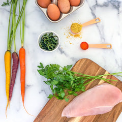 raw chicken breast and colourful carrots on a marble counter