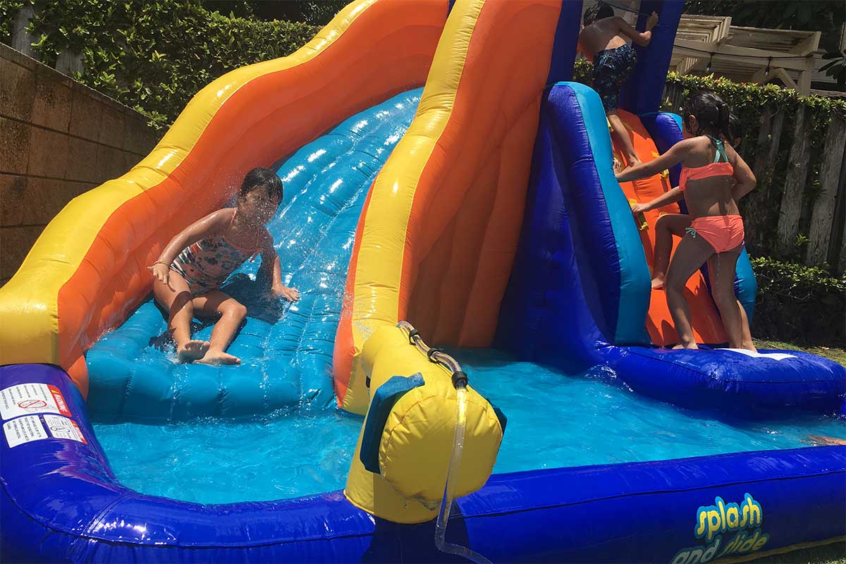 kids playing on an inflatable water slide in the backyard