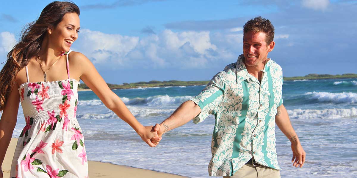 couple enjoying a stroll on the beach in a Hawaiian shirt and dress