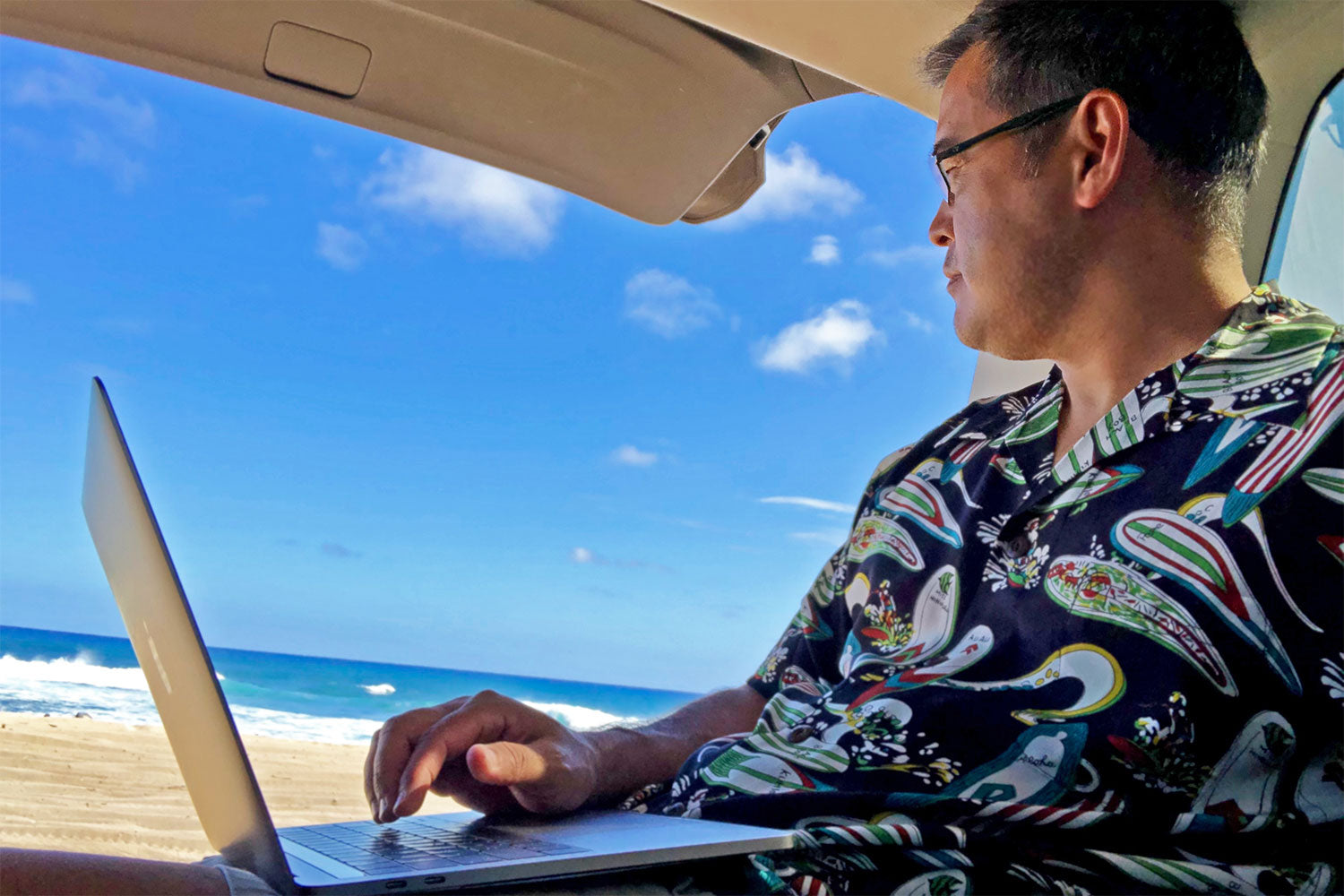 telecomuting on a laptop in the back of an SUV on the beach in a Hawaiian shirt