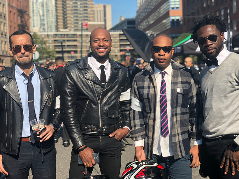 Four men dressed in vintage motorcycle clothing standing together posing for the camera