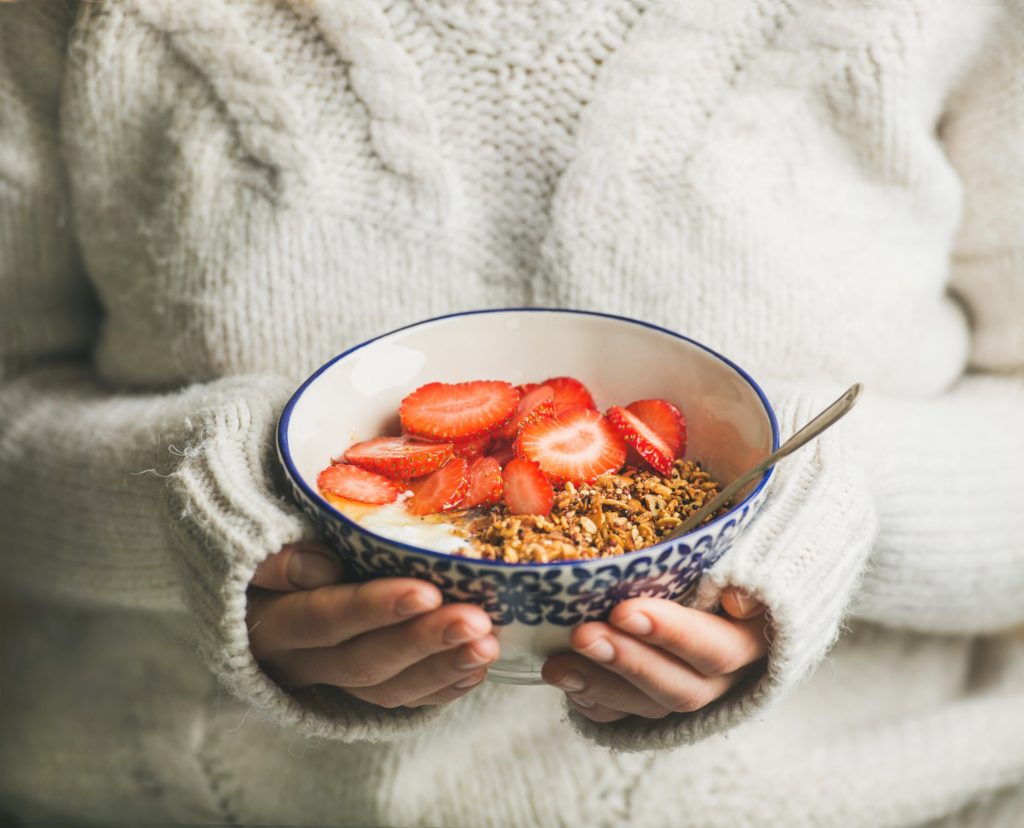 Healthy breakfast yogurt, granola, strawberry bowl in hands of woman