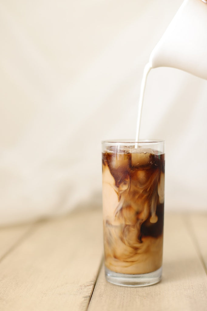 milk being poured into a glass of iced coffee