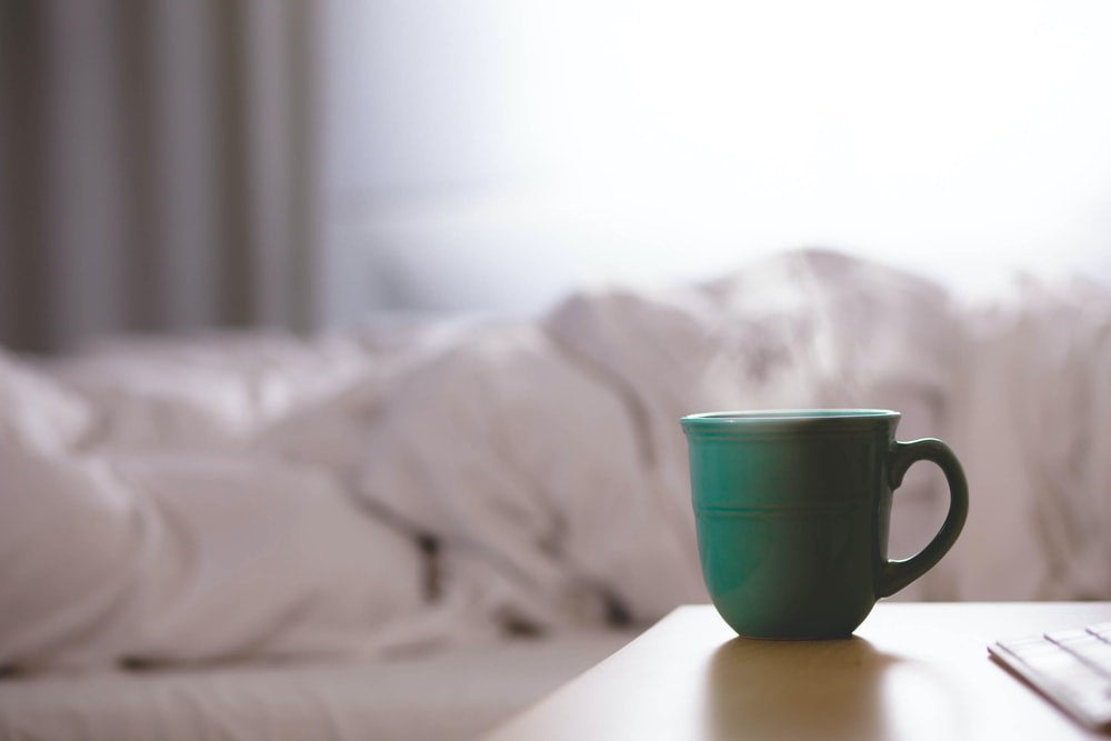 cup of coffee next to a bed