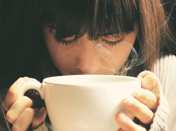 A woman smelling the scents from the hot cup of coffee she is holding. 