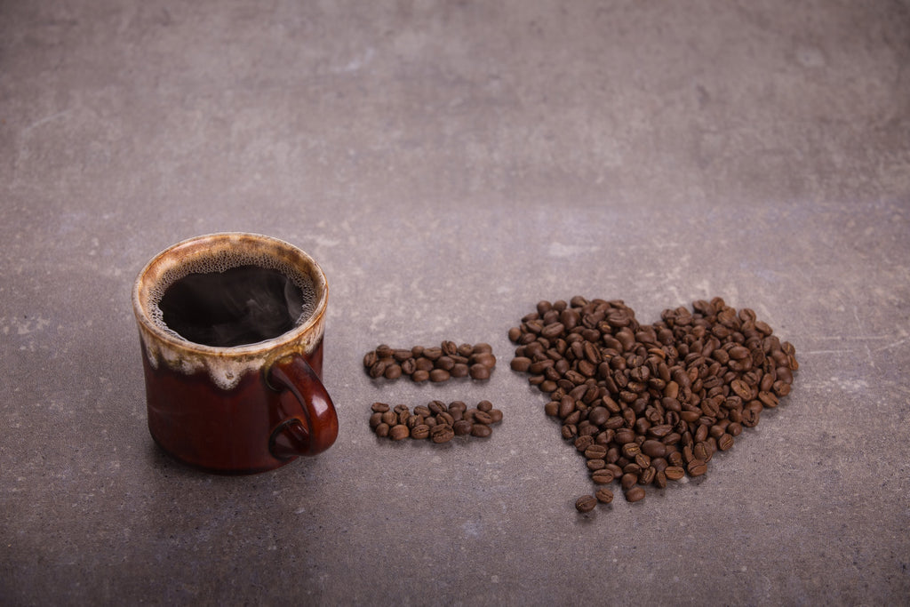 cup of coffee next to coffee beans in a heart shape