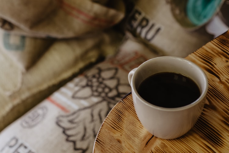 a cup of coffee next to a sack of coffee beans