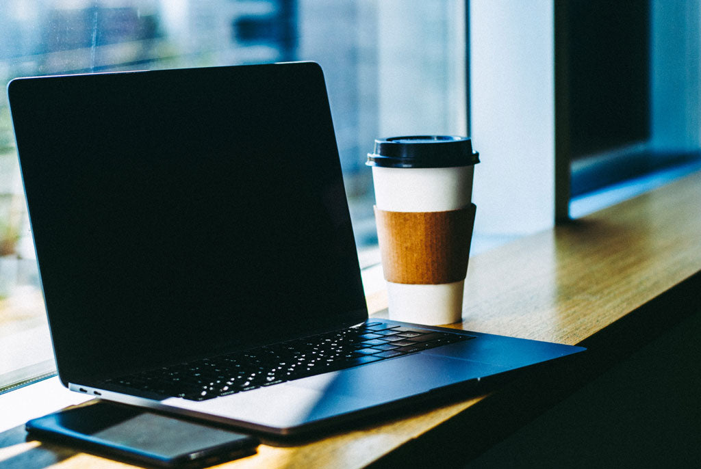 Laptop on table turned off next to coffee and mobile phone