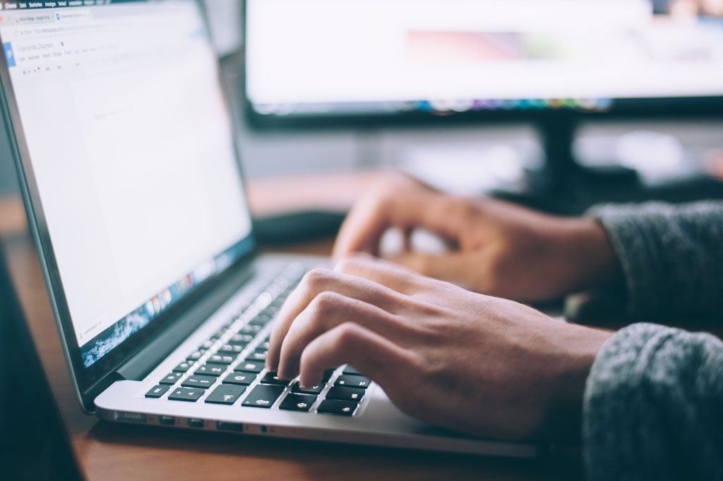 Person's hands typing on computer with bright screen