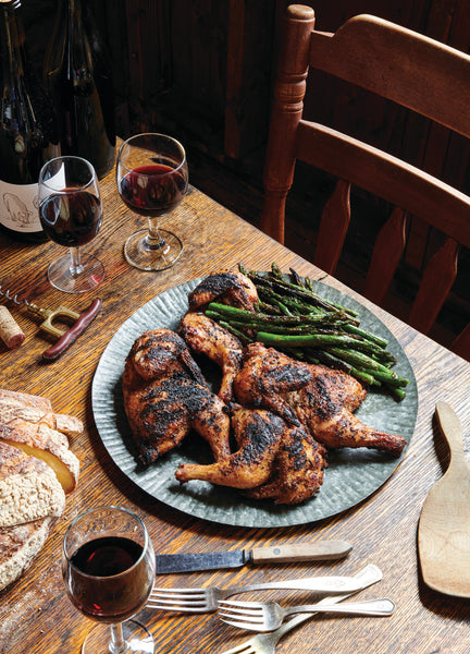 grilled chicken on a plate with asparagus and red in glasses on table with silverware