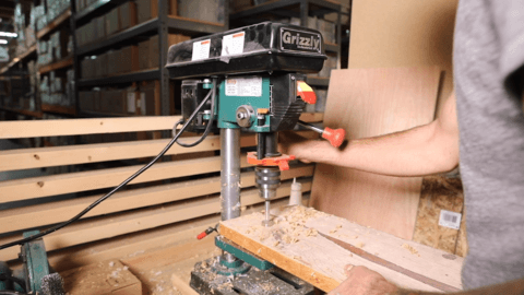 Person drilling a hole in a piece of wood with a drill press