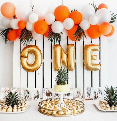 One year old birthday spread. Orange and white balloons decorated with pineapples and palm leaves.