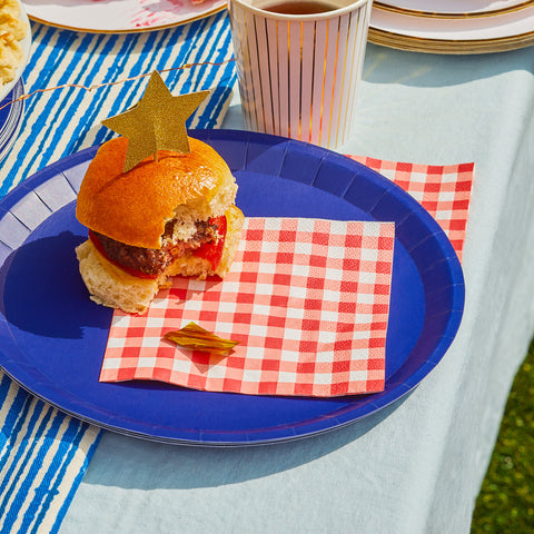 Burger with star topper on red gingham napkin and navy blue paper plate.