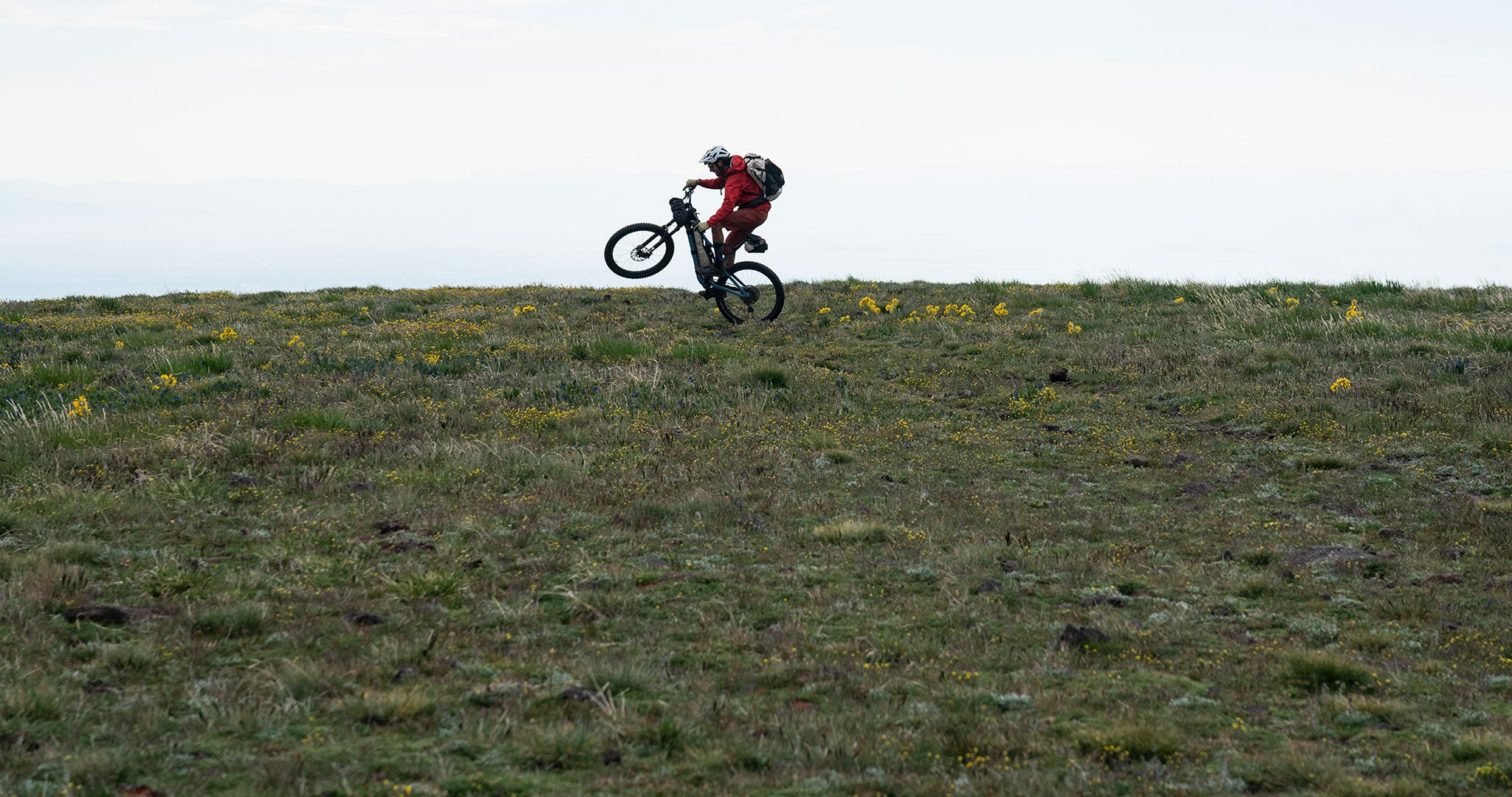 Bikepacker popping a wheelie in a field